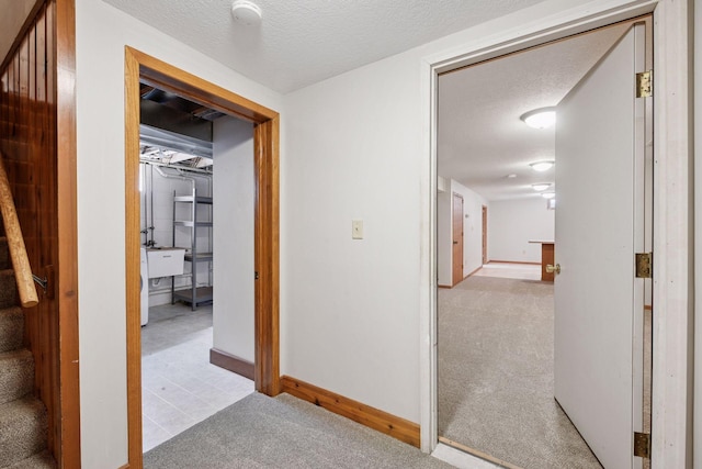 corridor featuring light colored carpet, stairway, a textured ceiling, and baseboards