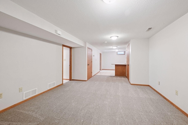 finished basement with light colored carpet, baseboards, and a textured ceiling