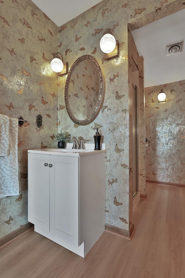 1379 7th Ave SE, Forest Lake, MN 55025 - bathroom with wallpapered walls, wood finished floors, vanity, a stall shower, and baseboards
