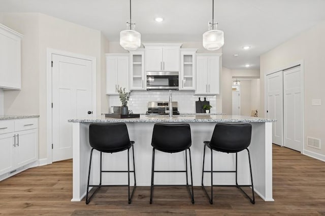 kitchen featuring appliances with stainless steel finishes, wood finished floors, white cabinets, tasteful backsplash, and a kitchen bar