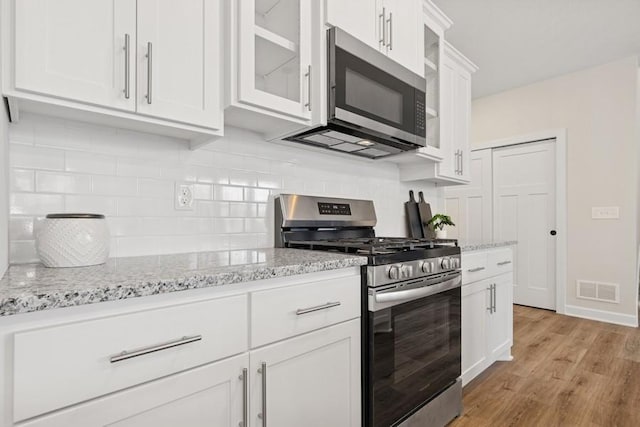 kitchen featuring appliances with stainless steel finishes, glass insert cabinets, white cabinets, tasteful backsplash, and light stone counters