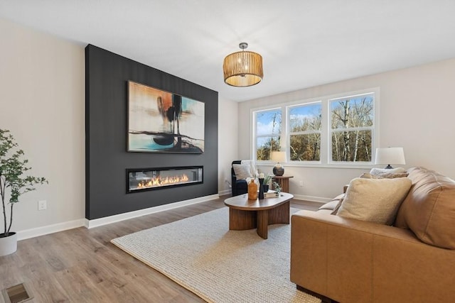 living area with light wood-type flooring, a glass covered fireplace, and baseboards