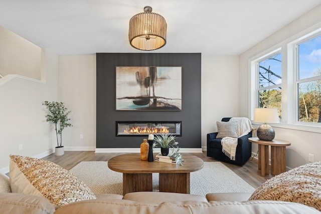 living room featuring wood finished floors, a glass covered fireplace, and baseboards