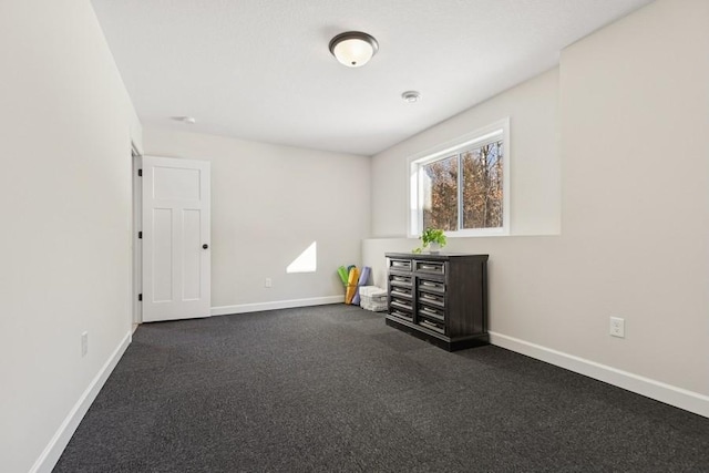 empty room featuring baseboards and dark colored carpet
