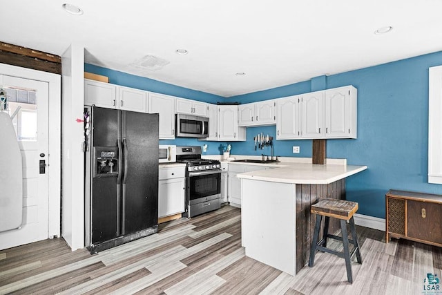 kitchen with appliances with stainless steel finishes, a peninsula, white cabinetry, light wood finished floors, and recessed lighting