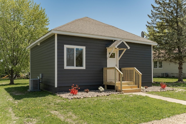 bungalow-style home featuring central air condition unit, a front yard, and a shingled roof