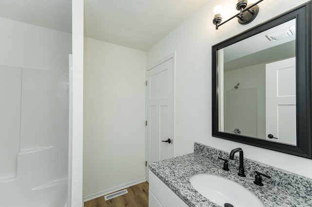 bathroom with wood finished floors, a shower, vanity, and baseboards