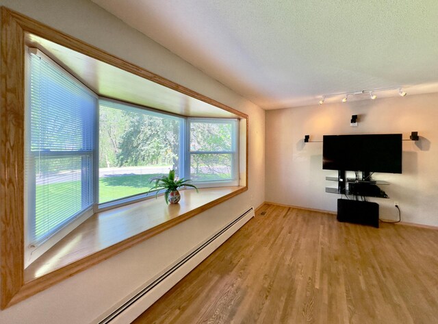 unfurnished living room featuring a baseboard radiator, light wood-type flooring, baseboards, a textured ceiling, and rail lighting