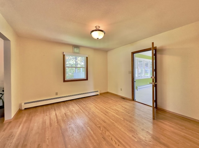 empty room with a baseboard heating unit, light wood-style flooring, baseboards, and a textured ceiling