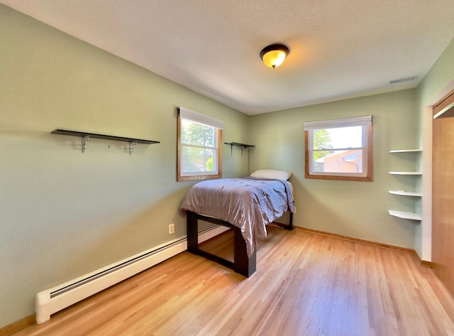 bedroom with a baseboard radiator, light wood-style floors, and baseboards