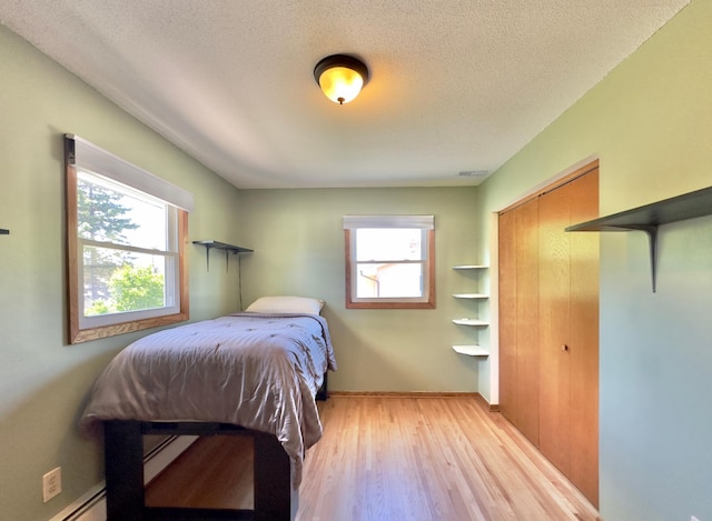 bedroom featuring light wood-style floors, baseboard heating, a textured ceiling, a closet, and baseboards