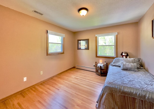 bedroom featuring a baseboard heating unit, multiple windows, light wood-style floors, and baseboards