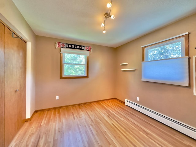 unfurnished bedroom featuring a baseboard radiator, multiple windows, light wood-type flooring, and a closet