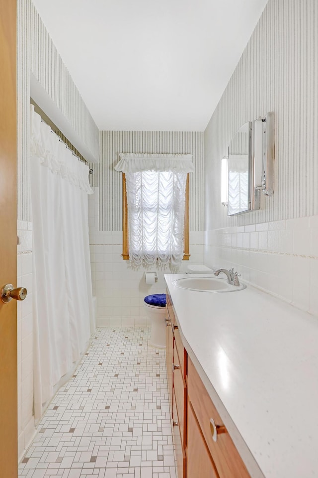 full bath featuring toilet, vanity, wallpapered walls, a shower with curtain, and tile walls