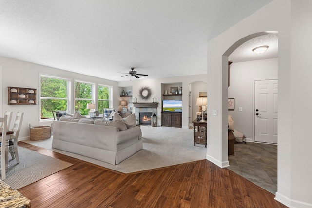 3121 Wild Flower Trl, Medina, MN 55340 - living area with arched walkways, a ceiling fan, a glass covered fireplace, wood-type flooring, and a textured ceiling