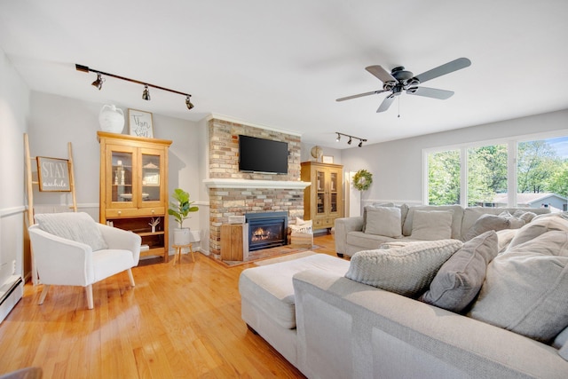 living area with track lighting, light wood-style flooring, ceiling fan, and a brick fireplace
