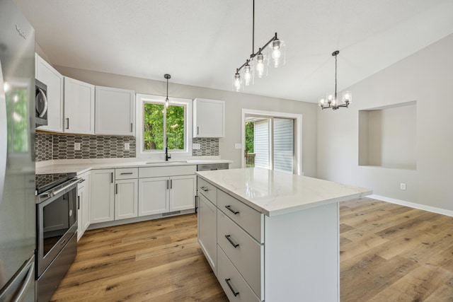 kitchen featuring appliances with stainless steel finishes, backsplash, light wood-style floors, lofted ceiling, and a center island