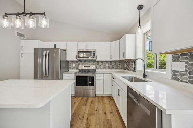 kitchen with stainless steel appliances, a sink, light wood finished floors, vaulted ceiling, and decorative backsplash