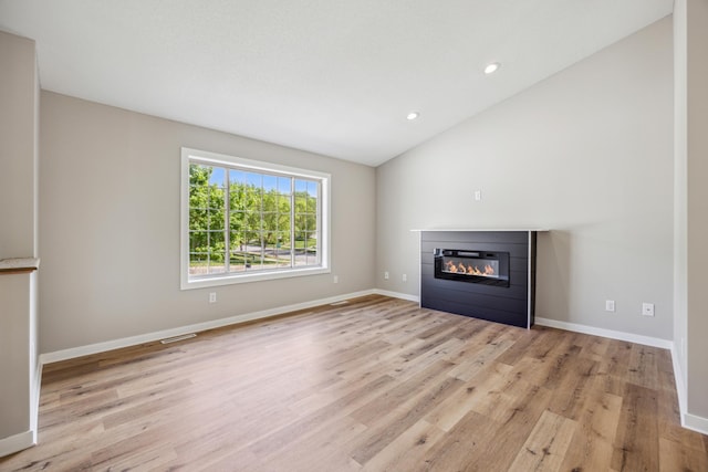 unfurnished living room featuring a glass covered fireplace, light wood-style flooring, vaulted ceiling, baseboards, and recessed lighting