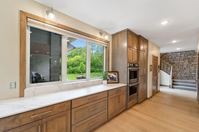 18565 Revere Ave, Spring Lake Twp, MN 55372 - kitchen featuring stainless steel double oven, light wood-style floors, brown cabinetry, recessed lighting, and light stone countertops