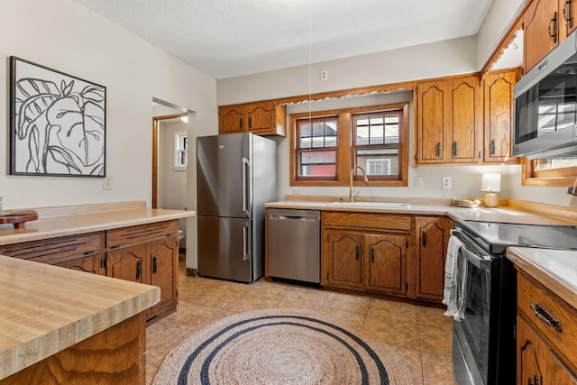 2901 Vincent Ave N, Minneapolis, MN 55411 - kitchen with stainless steel appliances, a sink, brown cabinetry, light countertops, and a textured ceiling