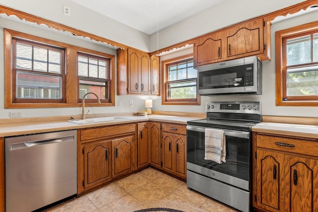 2901 Vincent Ave N, Minneapolis, MN 55411 - kitchen with stainless steel appliances, a sink, brown cabinets, light tile patterned floors, and light countertops