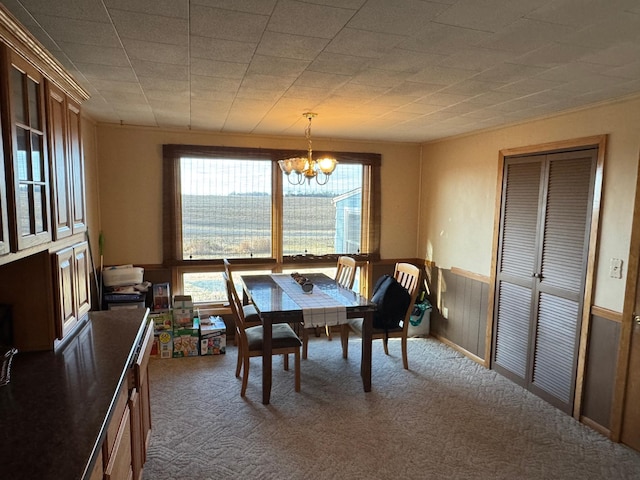 dining space with a chandelier, carpet floors, and a wainscoted wall