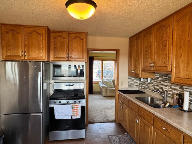 kitchen featuring appliances with stainless steel finishes, brown cabinets, a sink, backsplash, and a textured ceiling