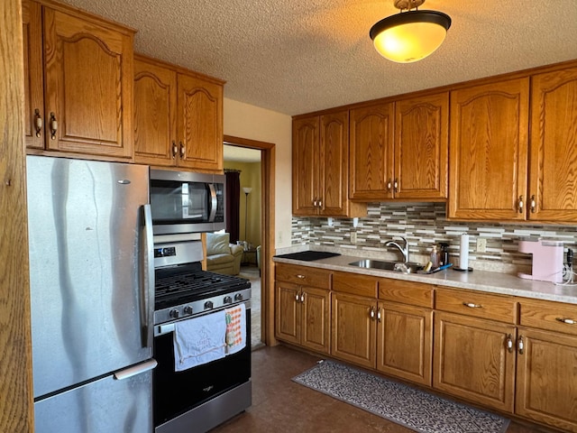 kitchen featuring stainless steel appliances, brown cabinetry, a sink, backsplash, and a textured ceiling