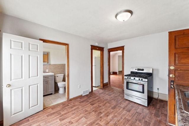 906 5th St E, Saint Paul, MN 55106 - kitchen with stainless steel range with gas cooktop, freestanding refrigerator, light wood-type flooring, a sink, and tile walls