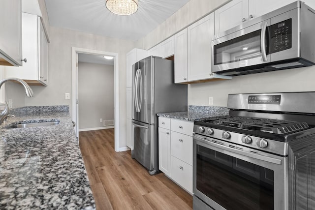 2237 Holloway Ave E, North Saint Paul, MN 55109 - kitchen featuring stainless steel appliances, a sink, light wood-style floors, white cabinets, and dark stone countertops