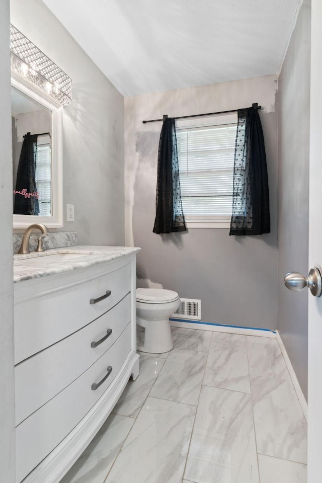 2237 Holloway Ave E, North Saint Paul, MN 55109 - half bath featuring vanity, plenty of natural light, toilet, and marble look tiles