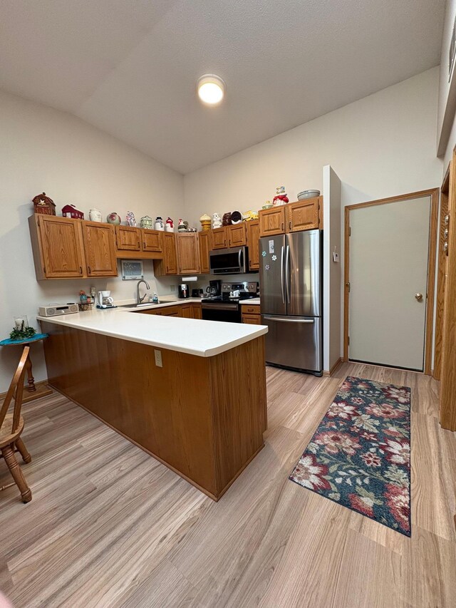 40 Broadway, Plainview, MN 55964 - kitchen with stainless steel appliances, a peninsula, brown cabinetry, vaulted ceiling, and light wood-type flooring