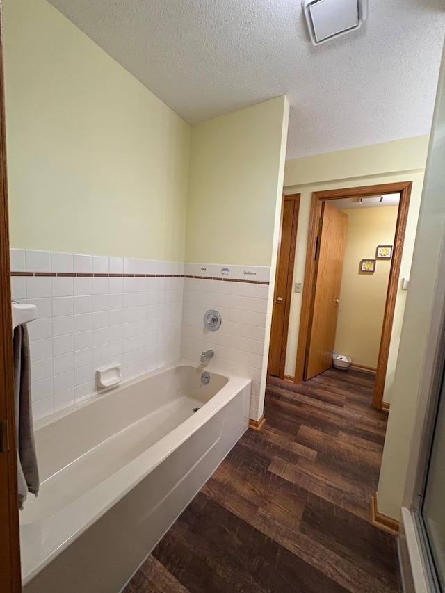 40 Broadway, Plainview, MN 55964 - bathroom featuring wood finished floors, a garden tub, tile walls, a textured ceiling, and a wainscoted wall