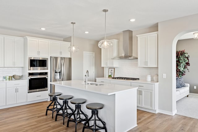 5107 Allen Dr, Woodbury, MN 55129 - kitchen with appliances with stainless steel finishes, wall chimney exhaust hood, a sink, light wood-type flooring, and a kitchen bar