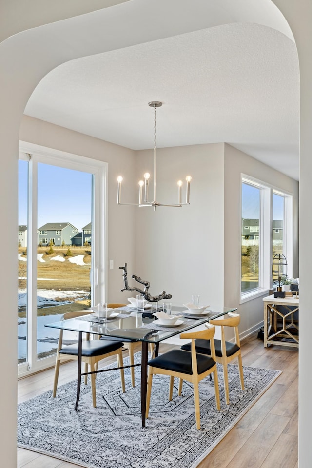 5107 Allen Dr, Woodbury, MN 55129 - dining area featuring arched walkways, a chandelier, light wood finished floors, and baseboards