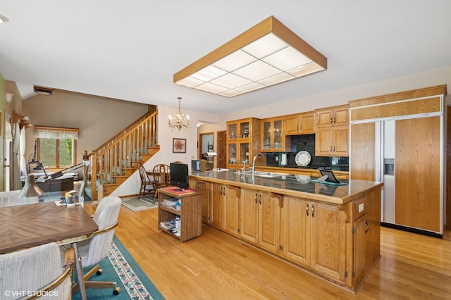 28075 Zuni St NW, Isanti, MN 55040 - kitchen with paneled refrigerator, a chandelier, light wood-style flooring, glass insert cabinets, and backsplash