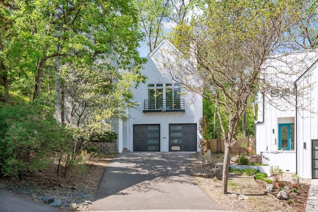 view of front of property featuring driveway, a balcony, an attached garage, and fence