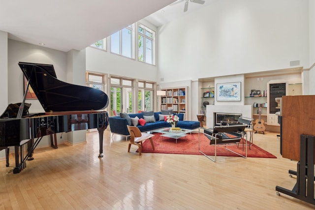 living area with a high ceiling, wood-type flooring, healthy amount of natural light, and a glass covered fireplace