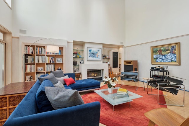 living area featuring a high ceiling, wood finished floors, and a glass covered fireplace