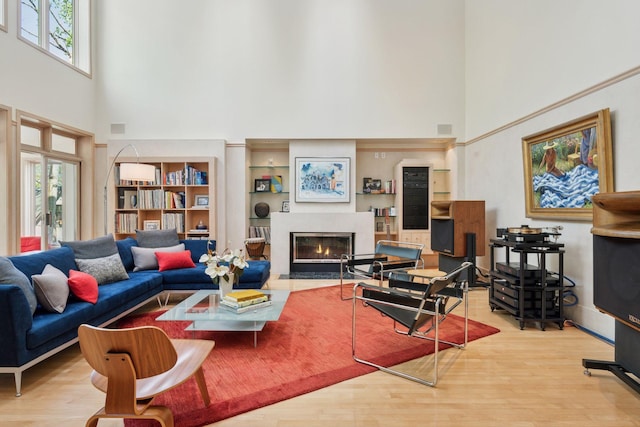 living area with a high ceiling, a fireplace with flush hearth, and wood finished floors