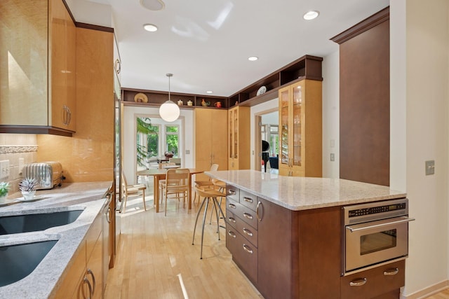 kitchen featuring oven, light wood-style flooring, light stone counters, pendant lighting, and recessed lighting