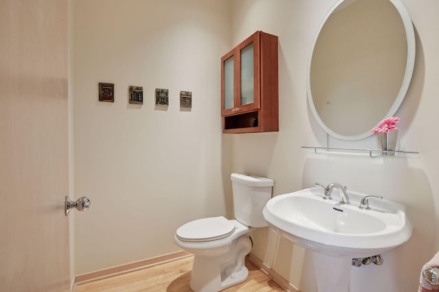 half bath featuring wood finished floors, toilet, and baseboards