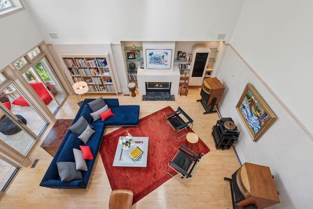 living area featuring a high ceiling, wood finished floors, built in features, and a lit fireplace
