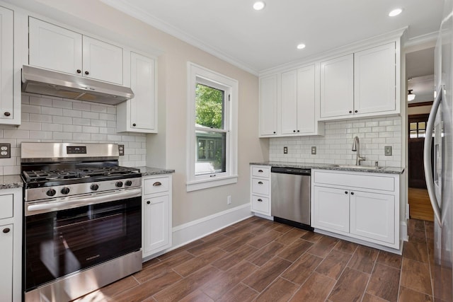 kitchen featuring appliances with stainless steel finishes, under cabinet range hood, a sink, baseboards, and crown molding
