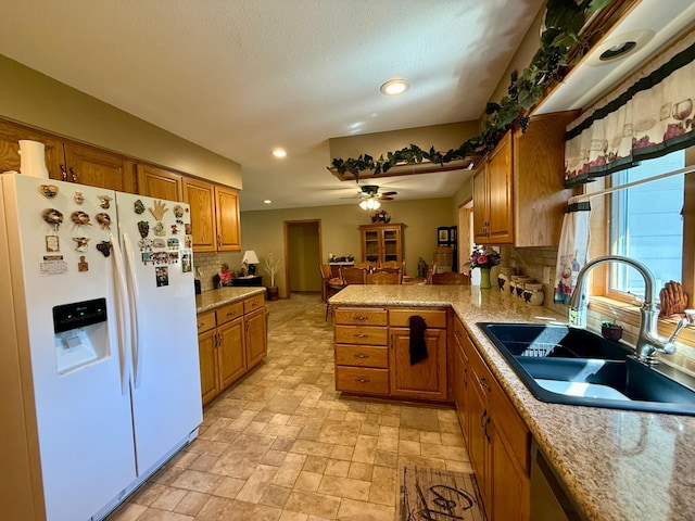 kitchen with white fridge with ice dispenser, a sink, brown cabinetry, ceiling fan, and recessed lighting
