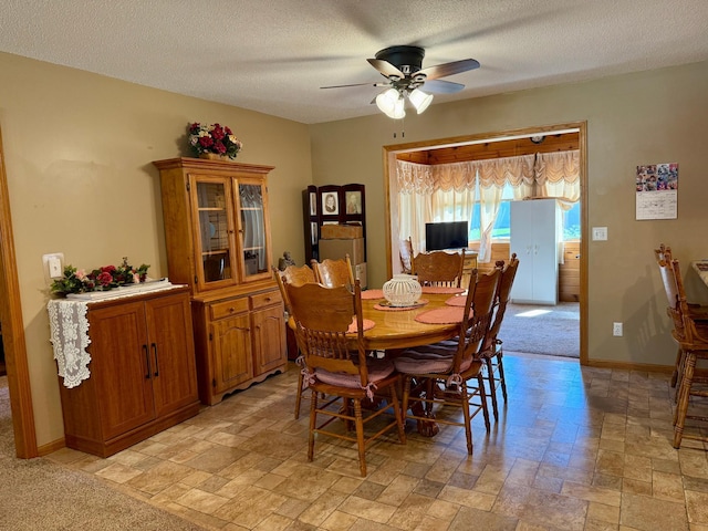 dining area featuring stone tile floors, ceiling fan, a textured ceiling, and baseboards