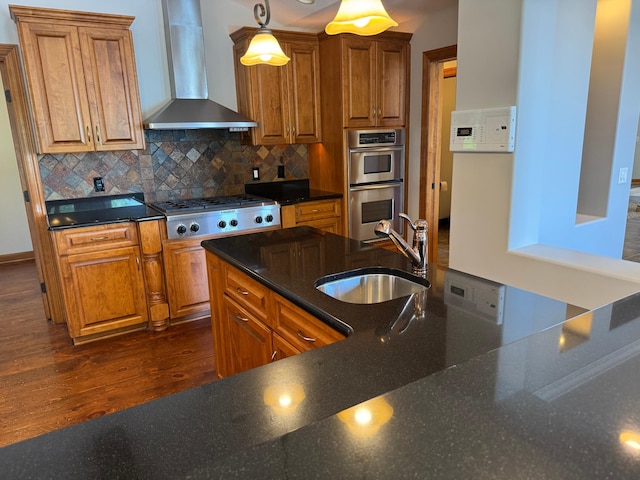 kitchen featuring a sink, wall chimney range hood, stainless steel appliances, and brown cabinetry