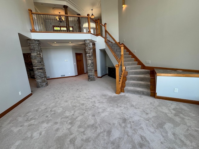 unfurnished living room featuring decorative columns, a towering ceiling, baseboards, carpet flooring, and stairway