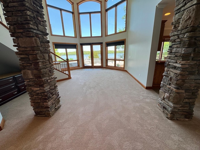 unfurnished living room featuring carpet floors, ornate columns, plenty of natural light, and a high ceiling